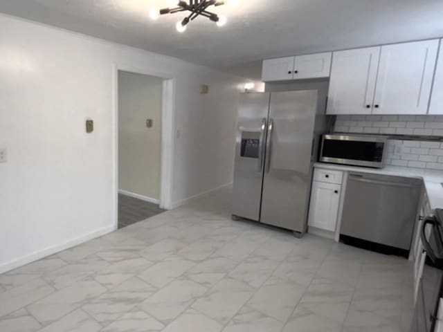 kitchen with white cabinets, marble finish floor, appliances with stainless steel finishes, light countertops, and backsplash