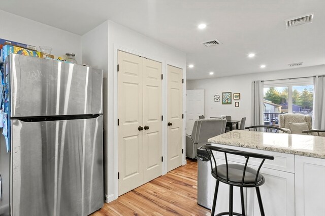 kitchen featuring stainless steel refrigerator, light stone countertops, a kitchen bar, white cabinets, and light wood-type flooring