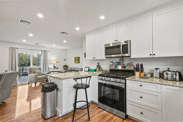 kitchen featuring kitchen peninsula, light hardwood / wood-style flooring, white cabinets, and appliances with stainless steel finishes