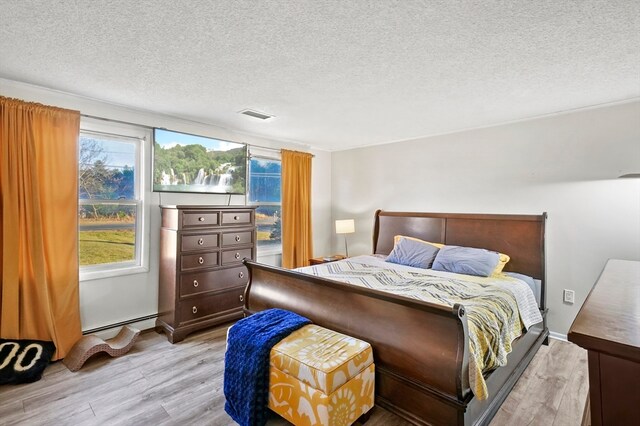 bedroom with light hardwood / wood-style flooring, a baseboard radiator, and a textured ceiling