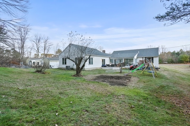 rear view of property with a playground, cooling unit, and a lawn