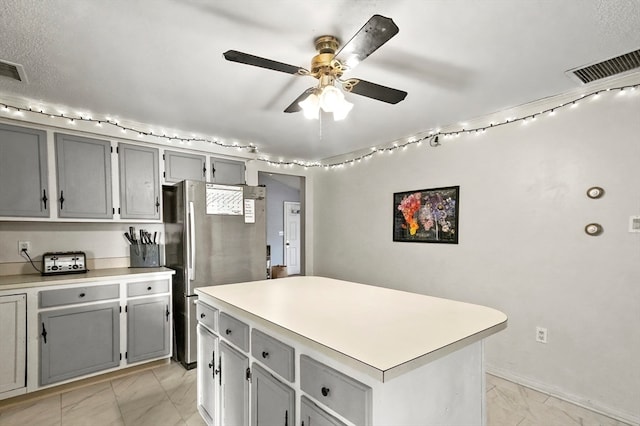 kitchen with stainless steel refrigerator, ceiling fan, a center island, and gray cabinetry