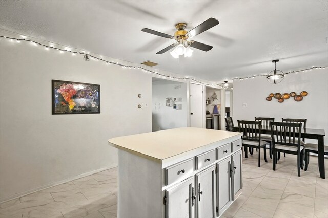 kitchen with gray cabinetry, ceiling fan, a kitchen island, and pendant lighting