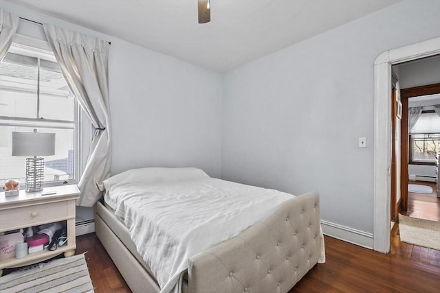 bedroom with dark wood-type flooring, ceiling fan, and a baseboard heating unit