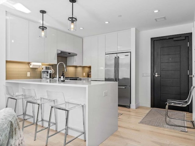 kitchen featuring modern cabinets, stainless steel built in fridge, light countertops, under cabinet range hood, and white cabinetry