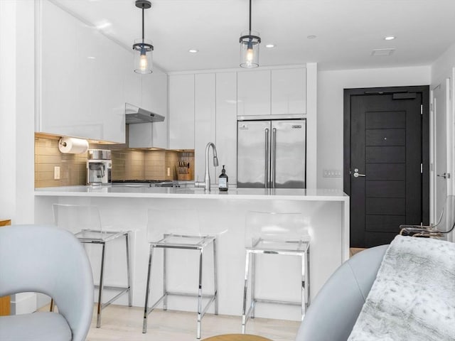 kitchen with modern cabinets, a breakfast bar area, built in refrigerator, light countertops, and pendant lighting