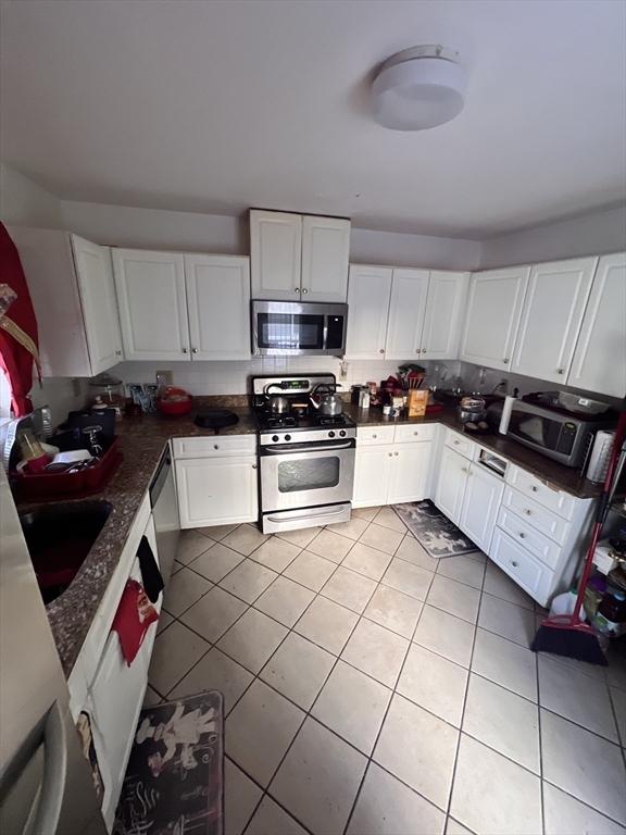 kitchen featuring sink, light tile patterned floors, appliances with stainless steel finishes, white cabinets, and dark stone counters