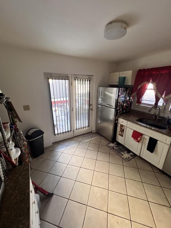 kitchen with white cabinets, sink, light tile patterned floors, and stainless steel refrigerator