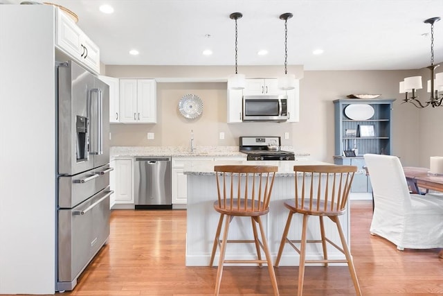 kitchen featuring a center island, a sink, light wood finished floors, stainless steel appliances, and white cabinetry
