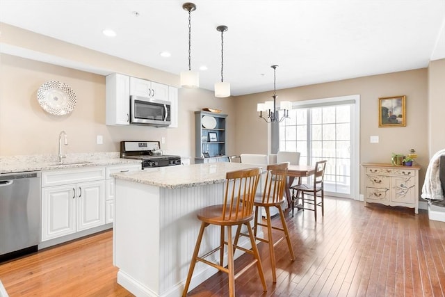 kitchen featuring light stone counters, a sink, light wood finished floors, stainless steel appliances, and white cabinetry