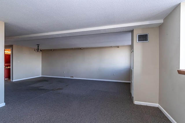 spare room with a notable chandelier, a textured ceiling, and dark carpet