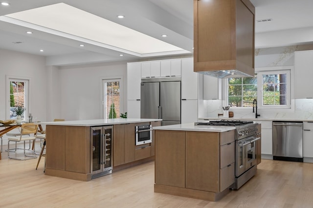 kitchen featuring plenty of natural light, high quality appliances, a kitchen island, white cabinetry, and wine cooler