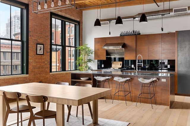 kitchen featuring sink, decorative light fixtures, a kitchen bar, light hardwood / wood-style floors, and brick wall