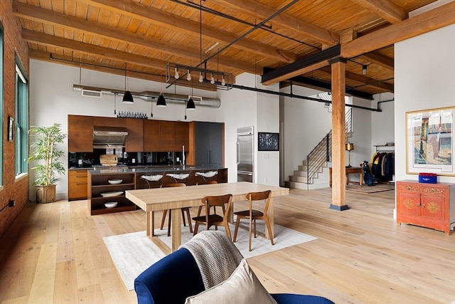 dining area featuring light hardwood / wood-style floors, wooden ceiling, beamed ceiling, and a high ceiling