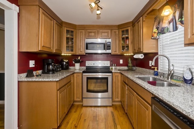 kitchen featuring sink, light stone countertops, light hardwood / wood-style floors, and appliances with stainless steel finishes