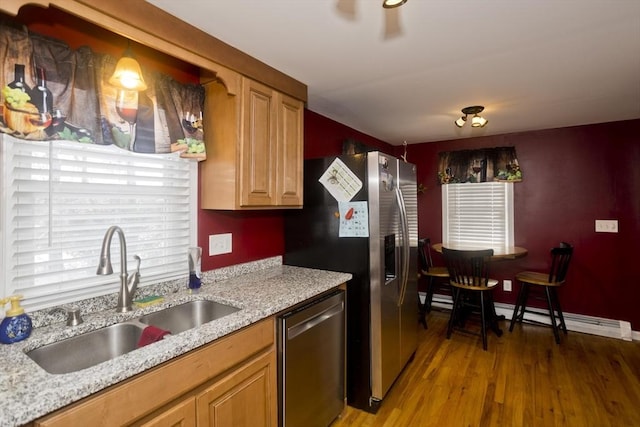 kitchen featuring appliances with stainless steel finishes, sink, hardwood / wood-style flooring, light stone counters, and baseboard heating