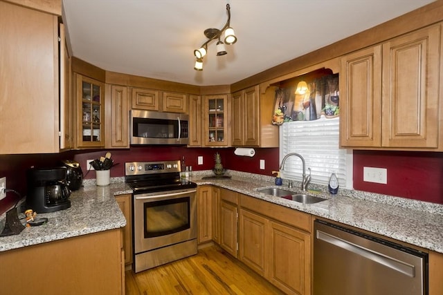 kitchen with stainless steel appliances, sink, light stone counters, and light hardwood / wood-style flooring