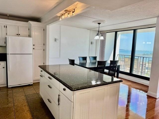 kitchen with freestanding refrigerator, pendant lighting, a center island, white cabinetry, and dark stone countertops