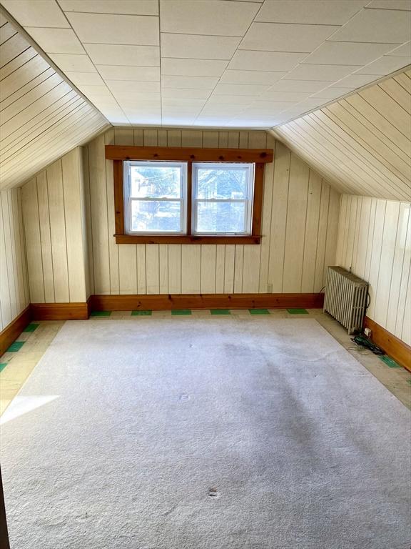 additional living space with lofted ceiling, radiator, light colored carpet, and wood walls