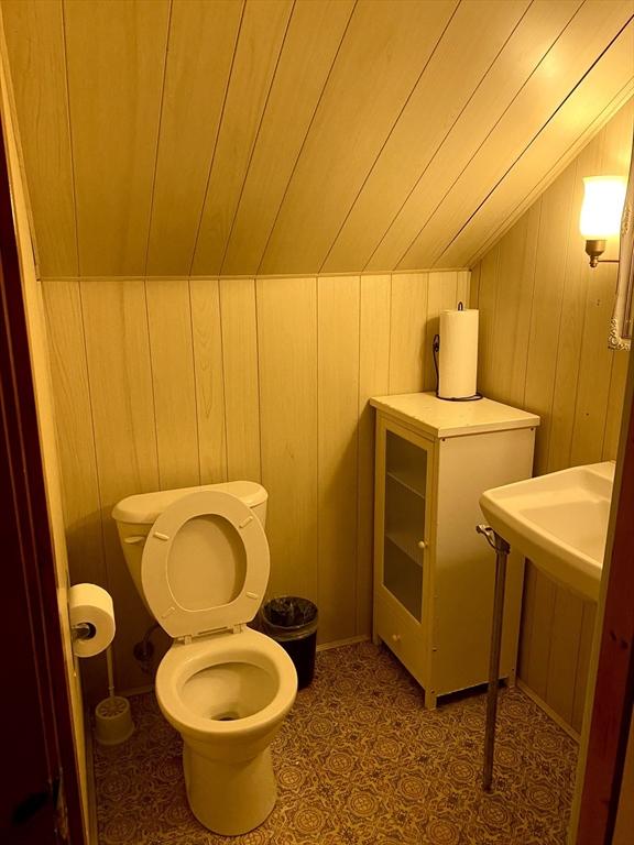 bathroom with wooden ceiling, toilet, vaulted ceiling, and wood walls