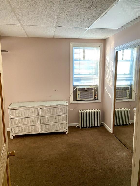 unfurnished room with cooling unit, dark carpet, and radiator heating unit