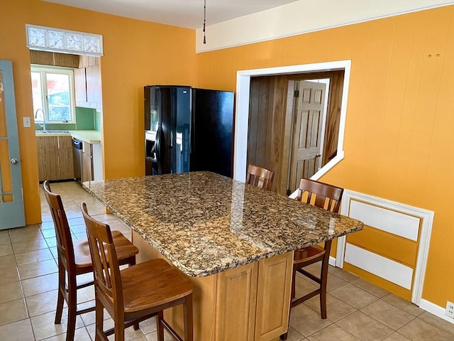 kitchen featuring sink, stone counters, a kitchen breakfast bar, black fridge, and stainless steel dishwasher