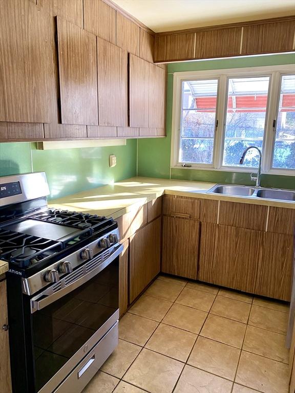 kitchen with light tile patterned floors, stainless steel range with gas cooktop, sink, and a wealth of natural light