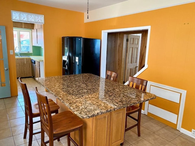 kitchen with black fridge with ice dispenser, sink, a breakfast bar area, stone countertops, and dishwasher