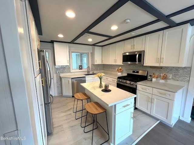kitchen featuring a sink, a kitchen island, a breakfast bar area, appliances with stainless steel finishes, and white cabinets
