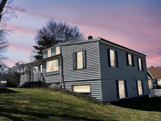 property exterior at dusk with a chimney, covered porch, and a yard
