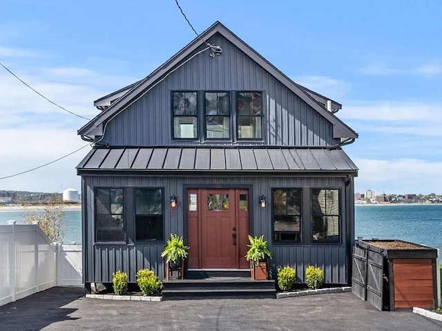 view of front of home with a standing seam roof, fence, a water view, and metal roof