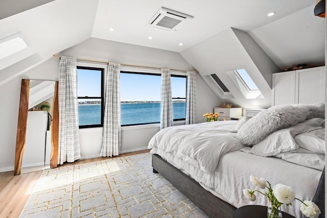 bedroom with visible vents, light wood-style flooring, vaulted ceiling with skylight, and multiple windows