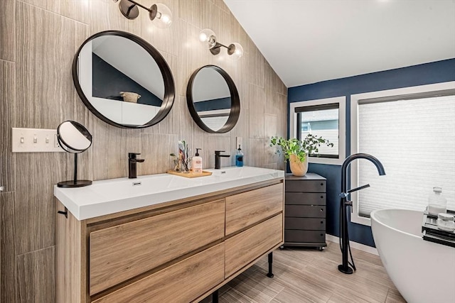 bathroom featuring double vanity, tile walls, baseboards, a freestanding bath, and a sink