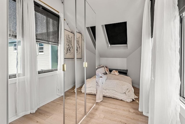 bedroom with baseboards, wood finished floors, and vaulted ceiling with skylight