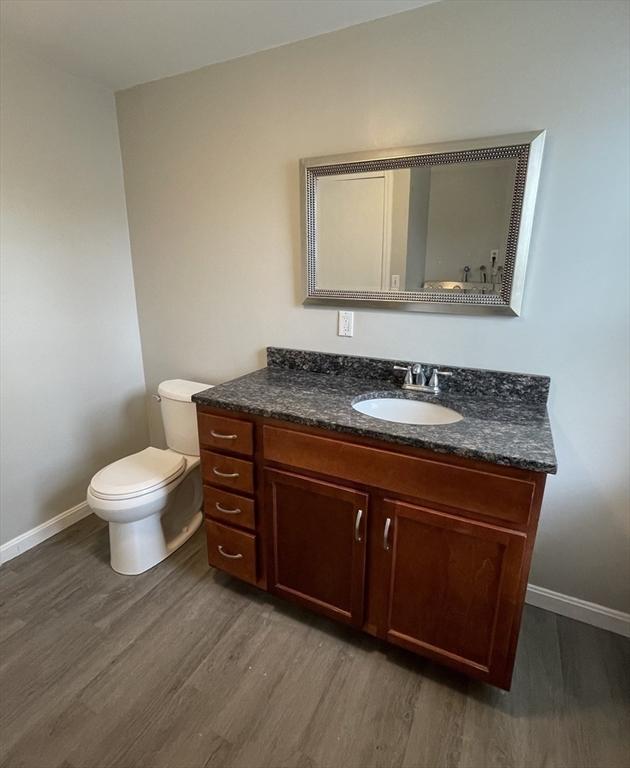 bathroom with wood finished floors, baseboards, vanity, and toilet