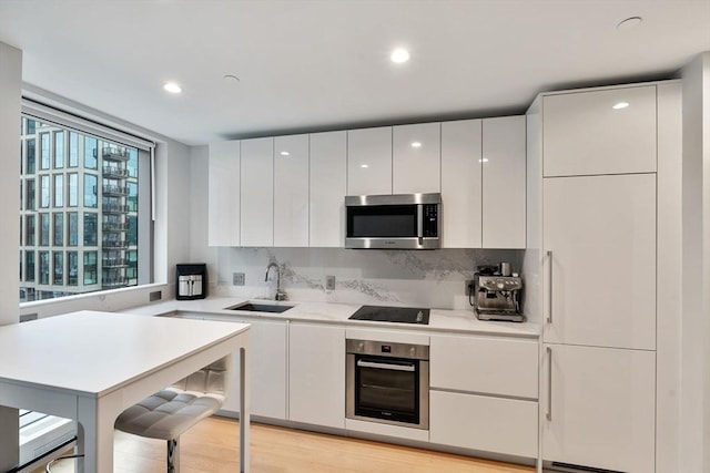 kitchen with sink, stainless steel appliances, decorative backsplash, white cabinets, and light wood-type flooring