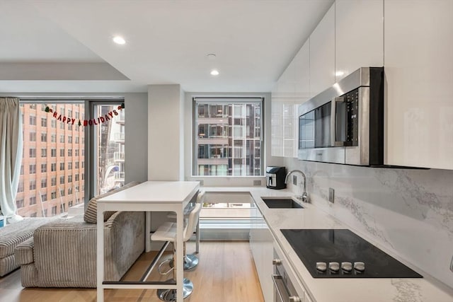 kitchen with white cabinets, sink, light stone countertops, light wood-type flooring, and black electric cooktop