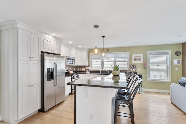 13 11th St W, Salisbury, MA 01952 - kitchen featuring appliances with stainless steel finishes, light wood-type flooring, a breakfast bar area, dark countertops, and white cabinetry