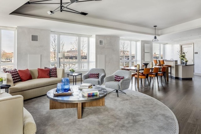 living room featuring a wealth of natural light, visible vents, a raised ceiling, and wood finished floors