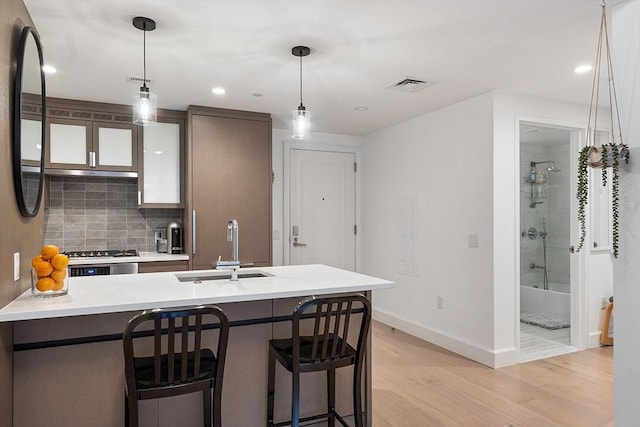 kitchen featuring visible vents, a sink, light wood-style floors, a kitchen bar, and backsplash