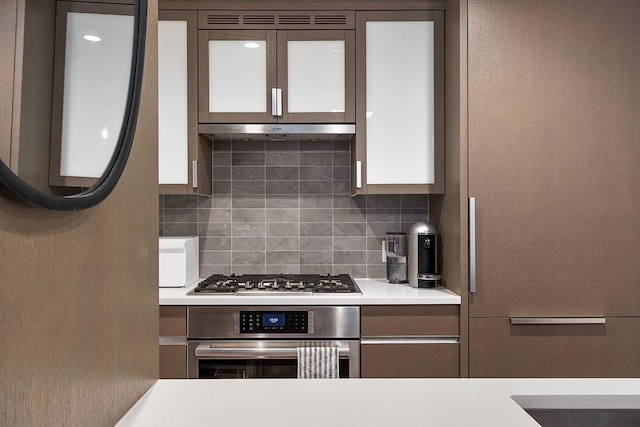 kitchen featuring under cabinet range hood, stainless steel appliances, white cabinets, light countertops, and decorative backsplash