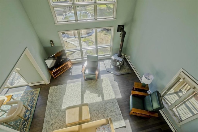 sitting room with baseboards, a wood stove, a towering ceiling, and wood finished floors