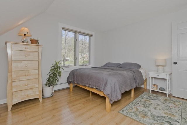 bedroom featuring a baseboard heating unit, light wood-style flooring, and vaulted ceiling