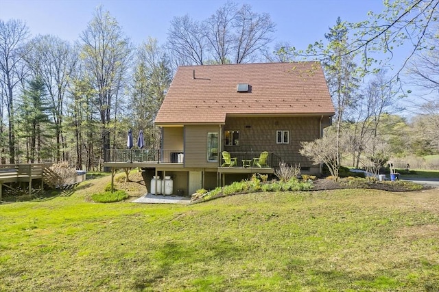 rear view of property with a deck, a shingled roof, and a lawn