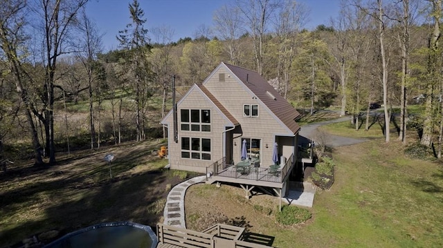 rear view of house with a yard, a deck, and a view of trees