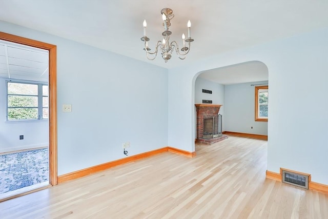 unfurnished living room with a chandelier, a fireplace, and light hardwood / wood-style flooring