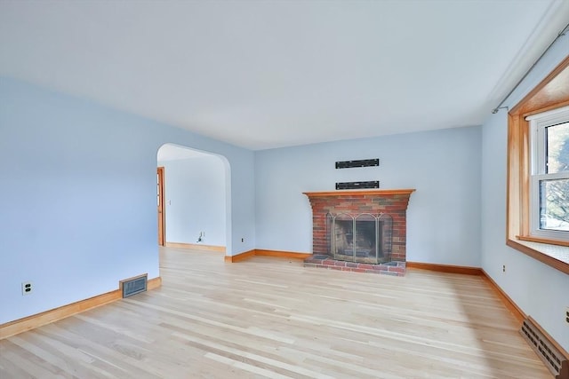 unfurnished living room featuring a brick fireplace, light hardwood / wood-style floors, and a baseboard heating unit