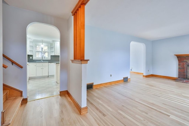 unfurnished living room with sink, a fireplace, and light hardwood / wood-style floors