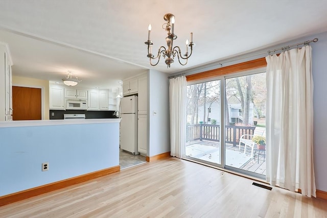 kitchen with pendant lighting, white cabinetry, white appliances, light hardwood / wood-style floors, and an inviting chandelier