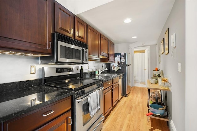 kitchen featuring stainless steel appliances, light wood-style flooring, a sink, recessed lighting, and dark stone counters